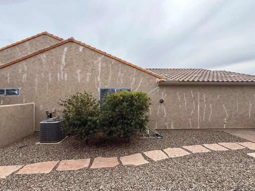 Side of a stucco home covered in white patch marks where cracks were sealed before painting