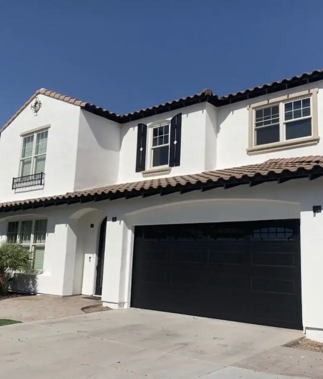 Two-story Spanish-style home painted bright white with black shutters and a black garage door